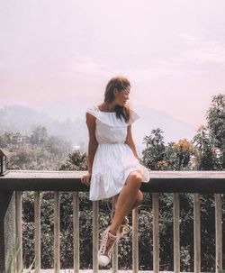 Woman sitting on railing against sky