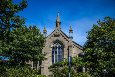 Low angle view of trees and building against blue sky