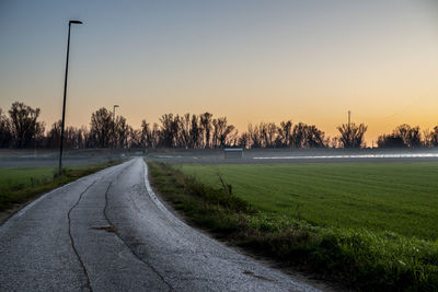 Road amidst field against clear sky during sunset