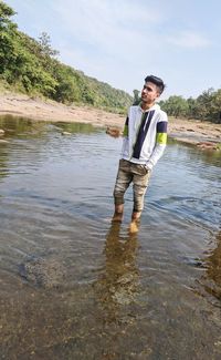 Portrait of young man standing in lake against sky