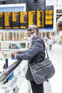 Contemplative businessman with laptop bag leaning on railing at station