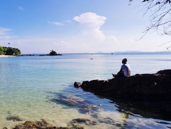 Man sitting on rock by sea against sky