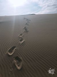 High angle view of footprints on sand at beach against sky