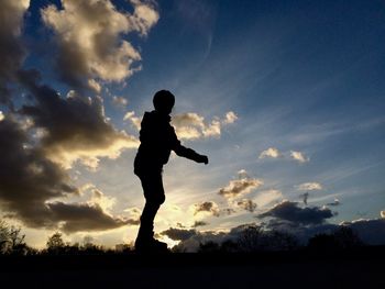 Silhouette boy standing on field against cloudy sky during sunset