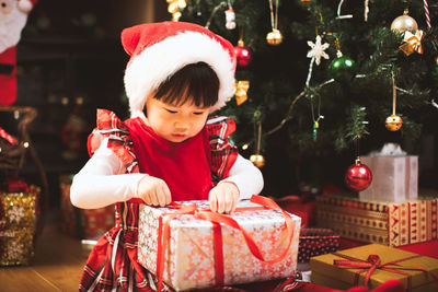 Girl opening gift while siting by christmas tree