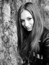 Portrait of beautiful young woman against tree trunk