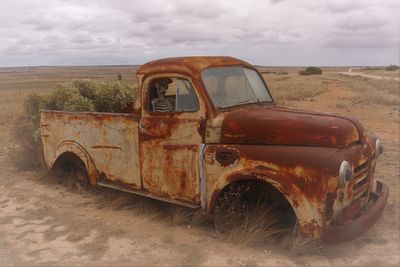Old rusty car on field against sky