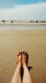 Low section of woman legs on beach against sky