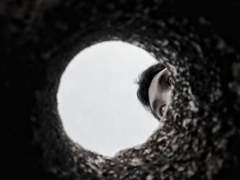 Cropped image of man against clear sky seen through hole