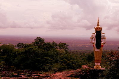 View of statue against trees and plants against cloudy sky