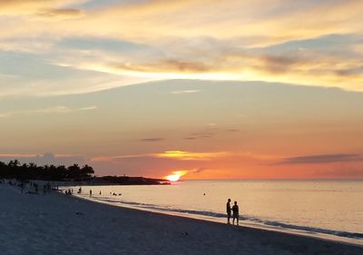 Silhouette people on beach against sky during sunset