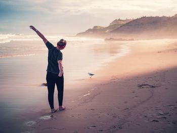 Rear view of woman with arms outstretched walking at beach