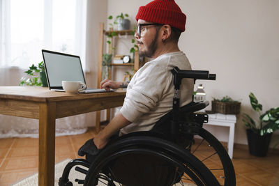 Thoughtful man in wheelchair with laptop at home