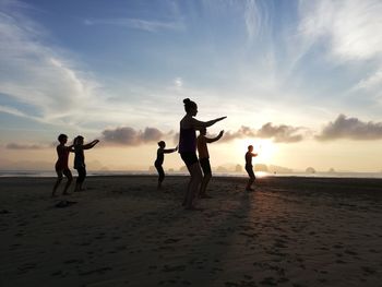 People exercising on beach against sky during sunset