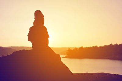 Silhouette of person sitting by lake during sunset