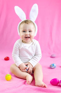 Happy baby girl with easter egg toy sitting on pink towel at home