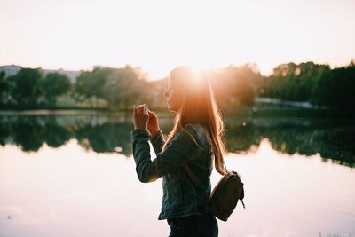 Woman standing by lake against sky during sunset