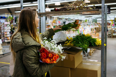 Girl stacks flowers on a shelf in a large flower shop