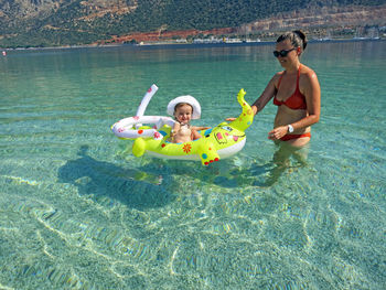 Smiling woman looking at daughter sitting on inflatable ring in sea