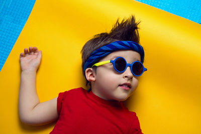 Child a boy in a red t shirt and sunglasses is lying on yellow paper resting at home