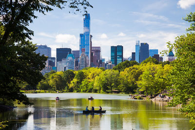 Scenic view of lake and trees against sky in city on sunny day at central park