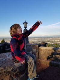 Full length of boy sitting on built structure against landscape