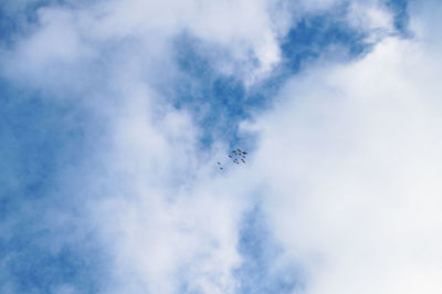 Low angle view of birds flying against cloudy sky