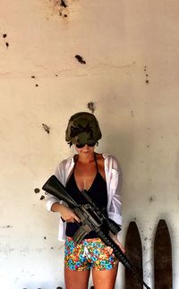 Woman holding ak-47 while standing against wall