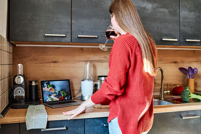 A young woman prepares a salad in the kitchen online and drinks red wine. cooking courses online