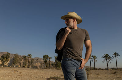 Adult man in cowboy hat on tabernas desert with palm trees against blue sky. almeria, spain