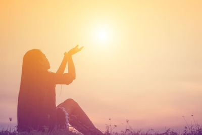 Silhouette woman sitting against sky during sunset