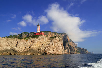 Lighthouse on cliff in front of sea against sky