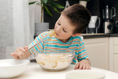 Cute boy licks a whisk with cake dough in the kitchen at home. time with children at home. 