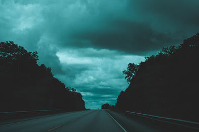 Road amidst trees against storm clouds