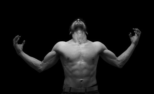 Shirtless man standing against black background