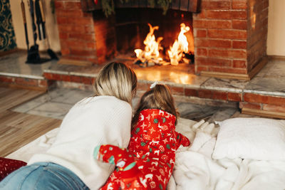 Happy mom and daughter are lying by the fireplace on christmas or new year's eve. rear view