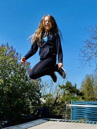 Low angle view of girl jumping against blue sky