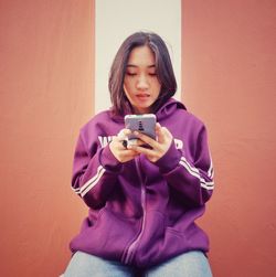 Portrait of young woman holding mobile phone against  wall