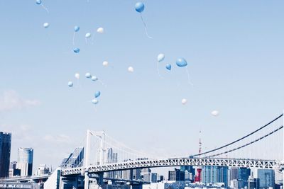 Low angle view of balloons flying above rainbow bridge against clear sky