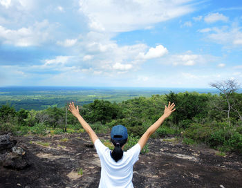 Rear view of woman with arms raised standing against landscape