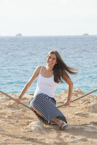 Young woman smiling at beach against sky