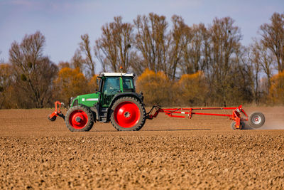 In front of a row of trees, a farmer is plowing a field with a tractor