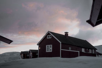 Houses on snow covered land against sky during sunset in norway