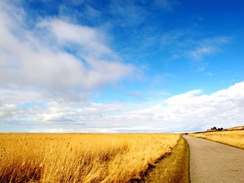 Empty road passing through field against cloudy sky