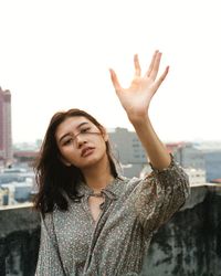 Portrait of young woman with arms raised standing against sky