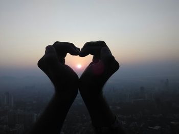 Cropped hands making heart shape with sun in between