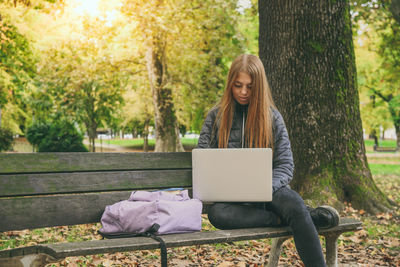 Girl study sitting on a bench in the park. teen using laptop, smartphone and reading a book outdoor.