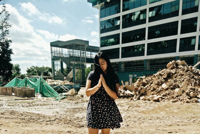Young woman with hands clasped standing against buildings