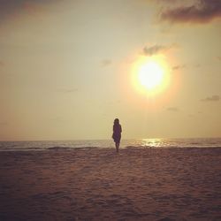 Rear view of woman walking on shore at beach against sky during sunset