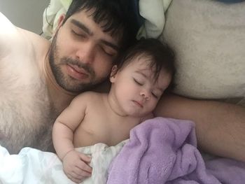 Shirtless father with daughter sleeping on bed
